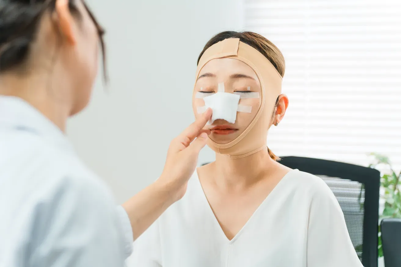 Plastic surgeon examining patient’s bandaged nose after rhinoplasty